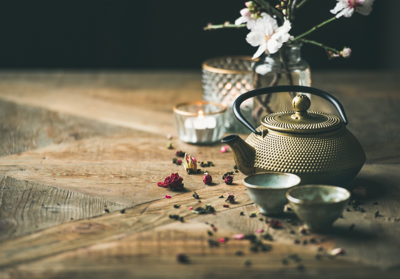 Traditional Asian tea ceremony arrangement. Golden iron teapot, cups, candles and almond blossom flowers over vintage wooden table background, copy space, selective focus